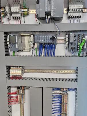 open electrical control cabinet filled with various industrial automation components. Several Programmable Logic Controllers (PLCs) with connected input/output modules are visible
